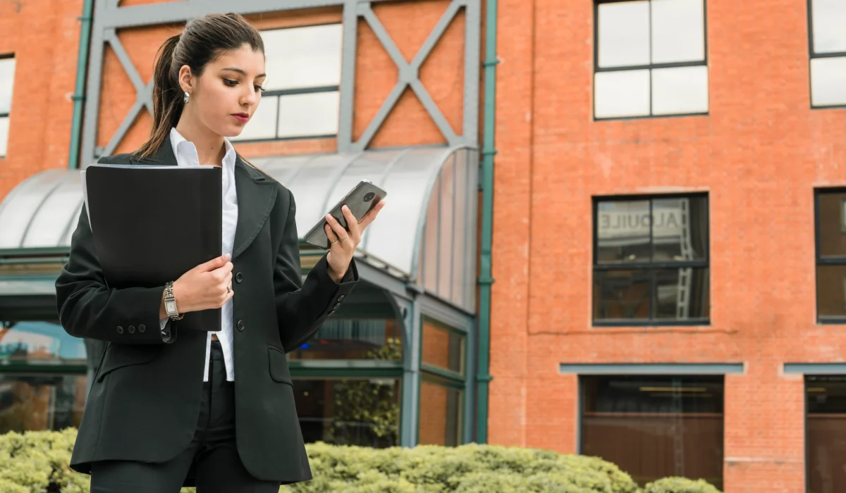 beautiful-young-woman-holding-folder-hand-looking-mobile-phone